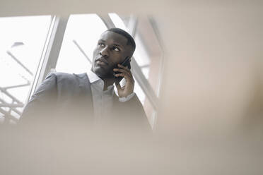 Portrait of young businessman in front of window on the phone - KNSF07423