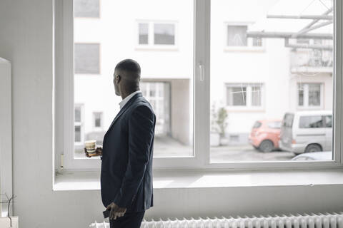 Geschäftsmann mit Pappbecher und Smartphone schaut aus dem Fenster, lizenzfreies Stockfoto
