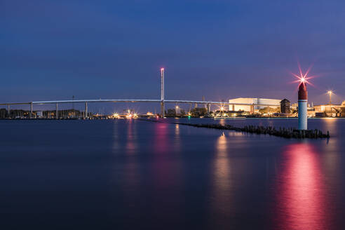 Deutschland, Mecklenburg-Vorpommern, Stralsund, Leuchtturm am Ende der Seebrücke in der Abenddämmerung mit Rügenbrücke im Hintergrund - WDF05748