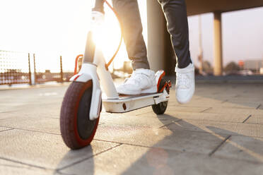 Crop view of man riding push scooter at sunset - JSRF00792