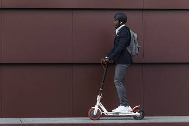 Businessman with backpack and cycling helmet on push scooter - JSRF00799