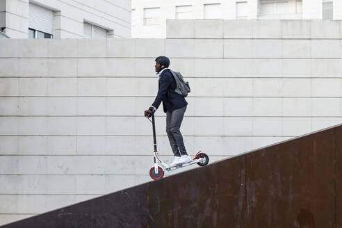 Businessman with backpack and cycling helmet on push scooter - JSRF00800