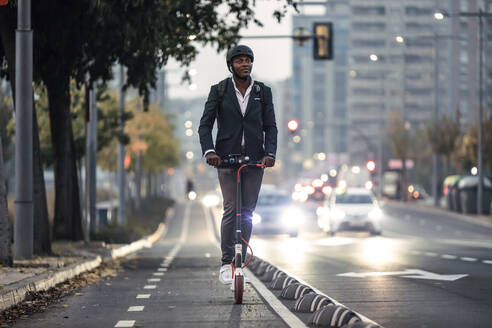 Porträt eines Geschäftsmannes, der abends auf dem Fahrradweg einen Motorroller fährt - JSRF00801