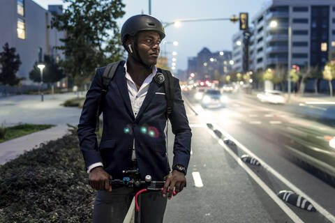 Porträt eines Geschäftsmannes mit Tretroller auf dem Fahrradweg am Abend, lizenzfreies Stockfoto