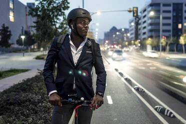 Porträt eines Geschäftsmannes mit Tretroller auf dem Fahrradweg am Abend - JSRF00803