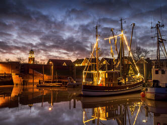 Deutschland, Niedersachsen, Landkreis Leer, Friesland, Ditzum, Weihnachtlich beleuchtetes Schiff in der Abenddämmerung - LAF02454