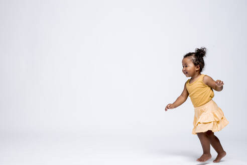 Happy little girl running barefoot in front of grey background - DAWF01262