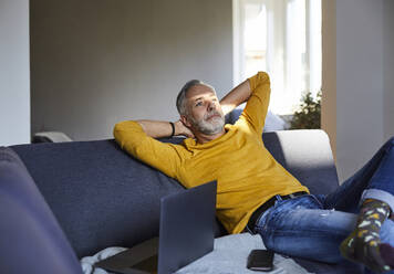 Mature man relaxing on couch at home - FMKF06099