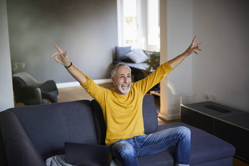 Älterer Mann sitzt auf der Couch zu Hause und jubelt - FMKF06101