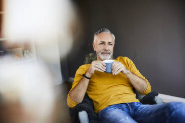 Entspannter reifer Mann zu Hause mit einer Tasse Kaffee - FMKF06102