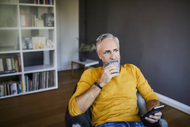 Entspannter reifer Mann zu Hause mit Handy und einer Tasse Kaffee - FMKF06105