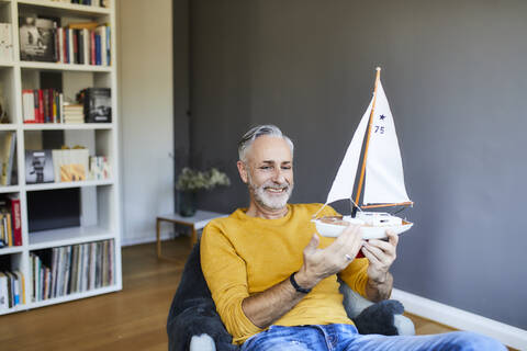 Lächelnder reifer Mann zu Hause mit Modell-Segelboot, lizenzfreies Stockfoto