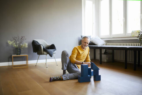 Mature man playing with building blocks on the floor at home - FMKF06112