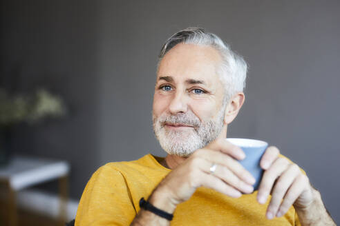Porträt eines lächelnden entspannten reifen Mannes zu Hause mit einer Tasse Kaffee - FMKF06123