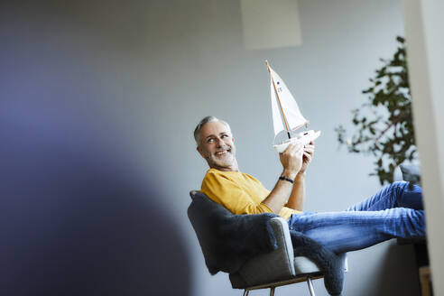Smiling mature man at home holding model sailboat - FMKF06124