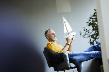 Smiling mature man at home holding model sailboat - FMKF06125