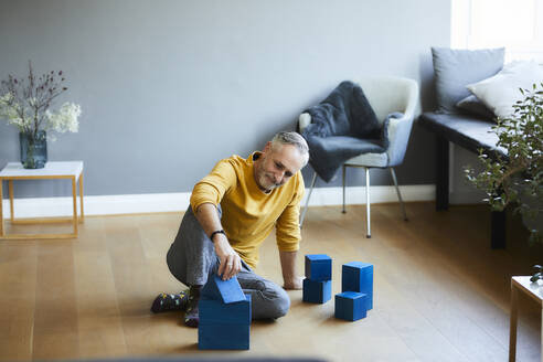 Mature man playing with building blocks on the floor at home - FMKF06126