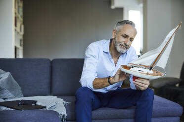 Mature man holding model sailboat at home - FMKF06130