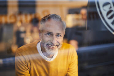 Porträt eines lächelnden reifen Mannes hinter einer Glasscheibe in einem Cafe - FMKF06143