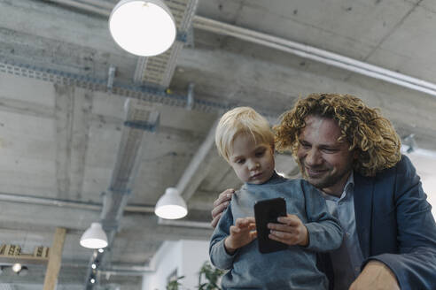 Geschäftsmann mit Sohn im Büro, der ein Mobiltelefon benutzt - KNSF07438