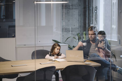 Casual businessman with two daughters working at desk in office stock photo