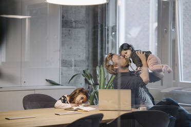 Lässiger Geschäftsmann mit zwei Töchtern bei der Arbeit am Schreibtisch im Büro - KNSF07452