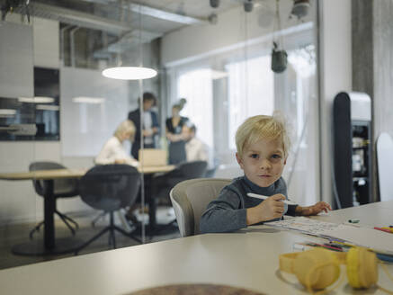 Porträt eines Jungen, der im Büro malt, während ein Geschäftsteam eine Besprechung abhält - KNSF07454