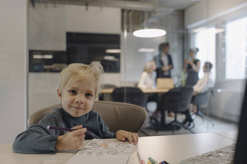 Porträt eines lächelnden Jungen, der in einem Büro mit einem Geschäftsteam eine Besprechung abhält - KNSF07456