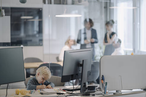 Junge malt im Büro mit einem Geschäftsteam, das eine Sitzung abhält - KNSF07461