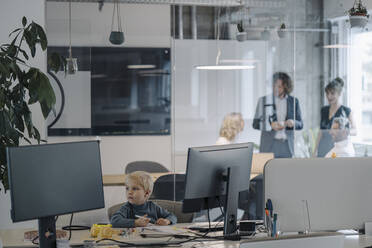 Junge malt im Büro mit einem Geschäftsteam, das eine Sitzung abhält - KNSF07465