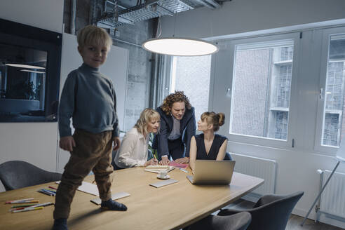 Boy standing on table in office with business team having a meeting - KNSF07473