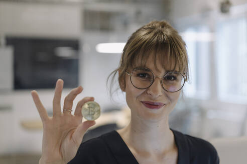 Portrait of businesswoman holding bitcoin in office - KNSF07485