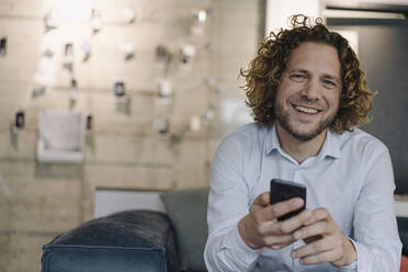 Porträt eines glücklichen Geschäftsmannes mit Mobiltelefon, der eine Pause im Büro macht - KNSF07489