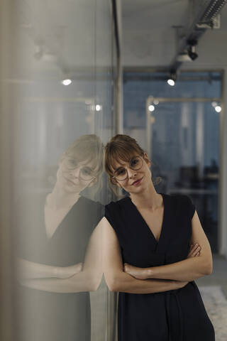 Portrait of businesswoman leaning against glass pane in office stock photo