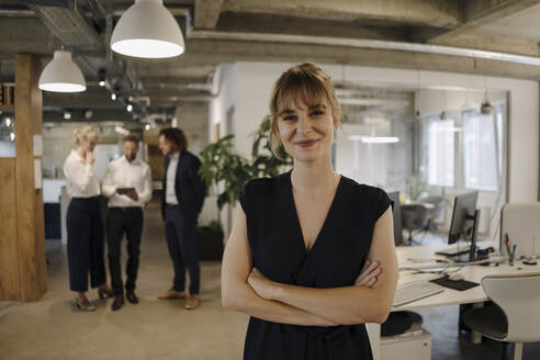 Portrait of confident businesswoman in office with colleagues in background - KNSF07548