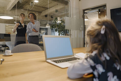 Geschäftsmann und Geschäftsfrau arbeiten an einem Projekt im Büro mit Mädchen mit Laptop im Vordergrund - KNSF07550
