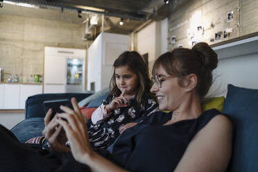 Woman and girl sitting on couch in office using smartphone - KNSF07557