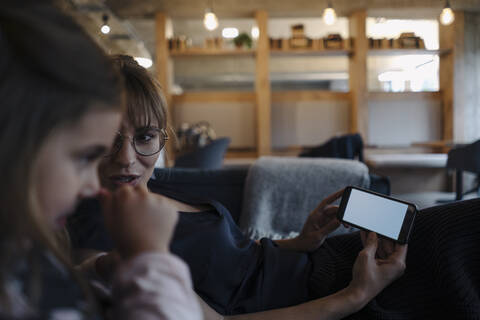 Frau und Mädchen sitzen auf der Couch im Büro und benutzen ein Smartphone, lizenzfreies Stockfoto