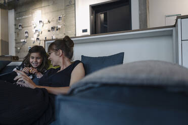 Happy woman and girl sitting on couch in office using smartphone - KNSF07559