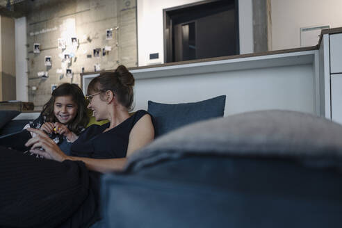 Glückliche Frau und Mädchen sitzen auf der Couch im Büro und benutzen ein Smartphone - KNSF07559