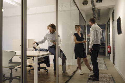 Geschäftsmann und Geschäftsfrau unterhalten sich im Büro mit einem Kollegen, der Kaffee zubereitet, lizenzfreies Stockfoto