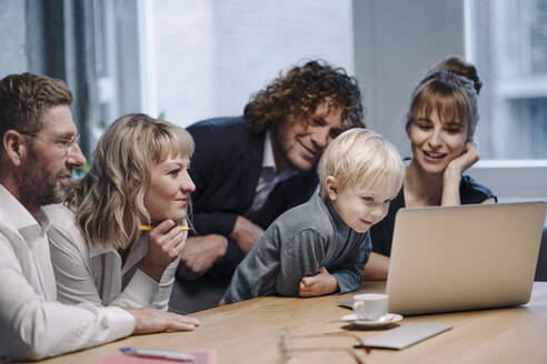 Geschäftsteam mit einem Jungen, der im Büro auf einen Laptop schaut - KNSF07572