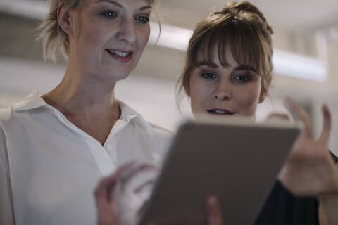 Zwei Geschäftsfrauen bei einer Besprechung im Büro, die sich ein Tablet teilen, lizenzfreies Stockfoto