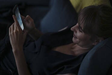 Lächelnde Frau mit Handy auf der Couch - KNSF07590