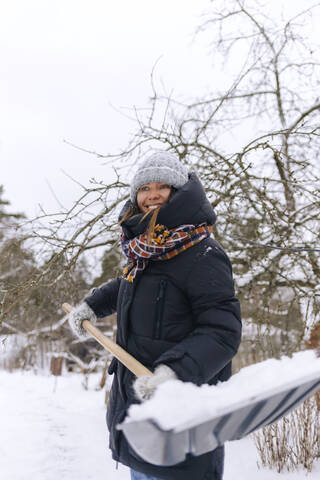 Porträt einer lächelnden Frau mit Schneeschaufel, lizenzfreies Stockfoto