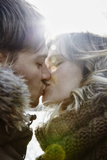 Küssendes junges Paar im Winter bei Gegenlicht - ANHF00149