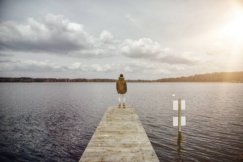 Rückenansicht eines jungen Mannes, der auf einem Steg steht und auf den See schaut - ANHF00153