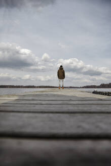 Back view of young man standing on a jetty looking at lake - ANHF00154