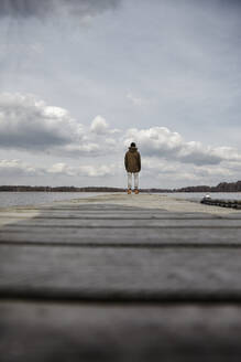 Rückenansicht eines jungen Mannes, der auf einem Steg steht und auf den See schaut - ANHF00154