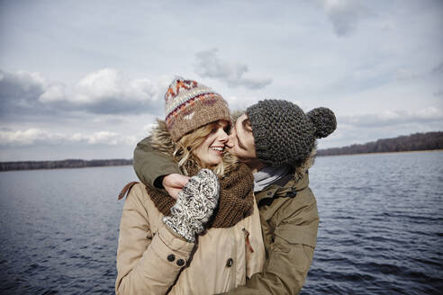 Young man kissing his girlfriend in front of a lake - ANHF00159